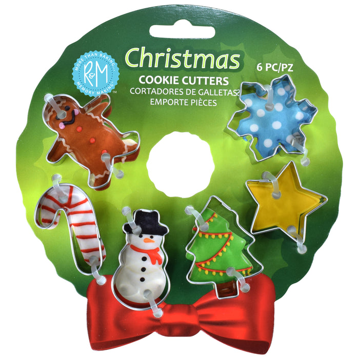 A 6-piece set of Christmas cookie cutters on a green circular backing card. The set includes a gingerbread man, snowman, candy cane, Christmas tree, snowflake, and star-shaped cutters, with a red bow at the bottom of the card.